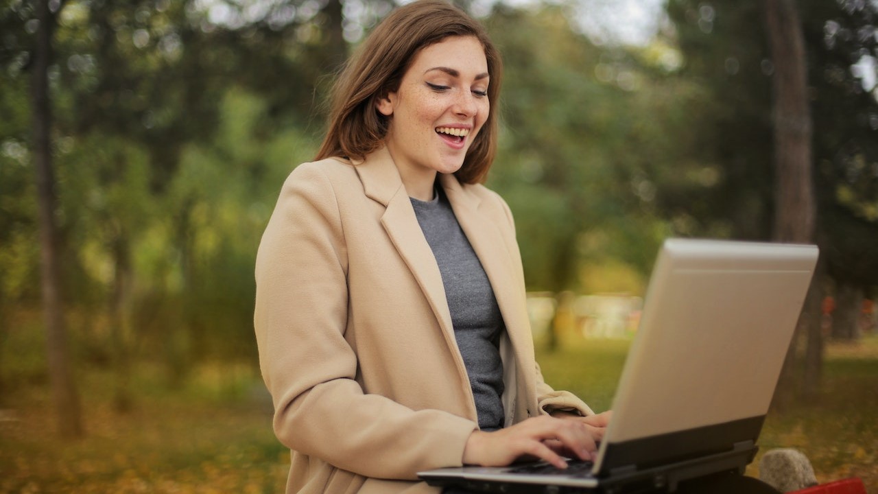 happy girl sitting in park working on computer-Andrea Piacquadio